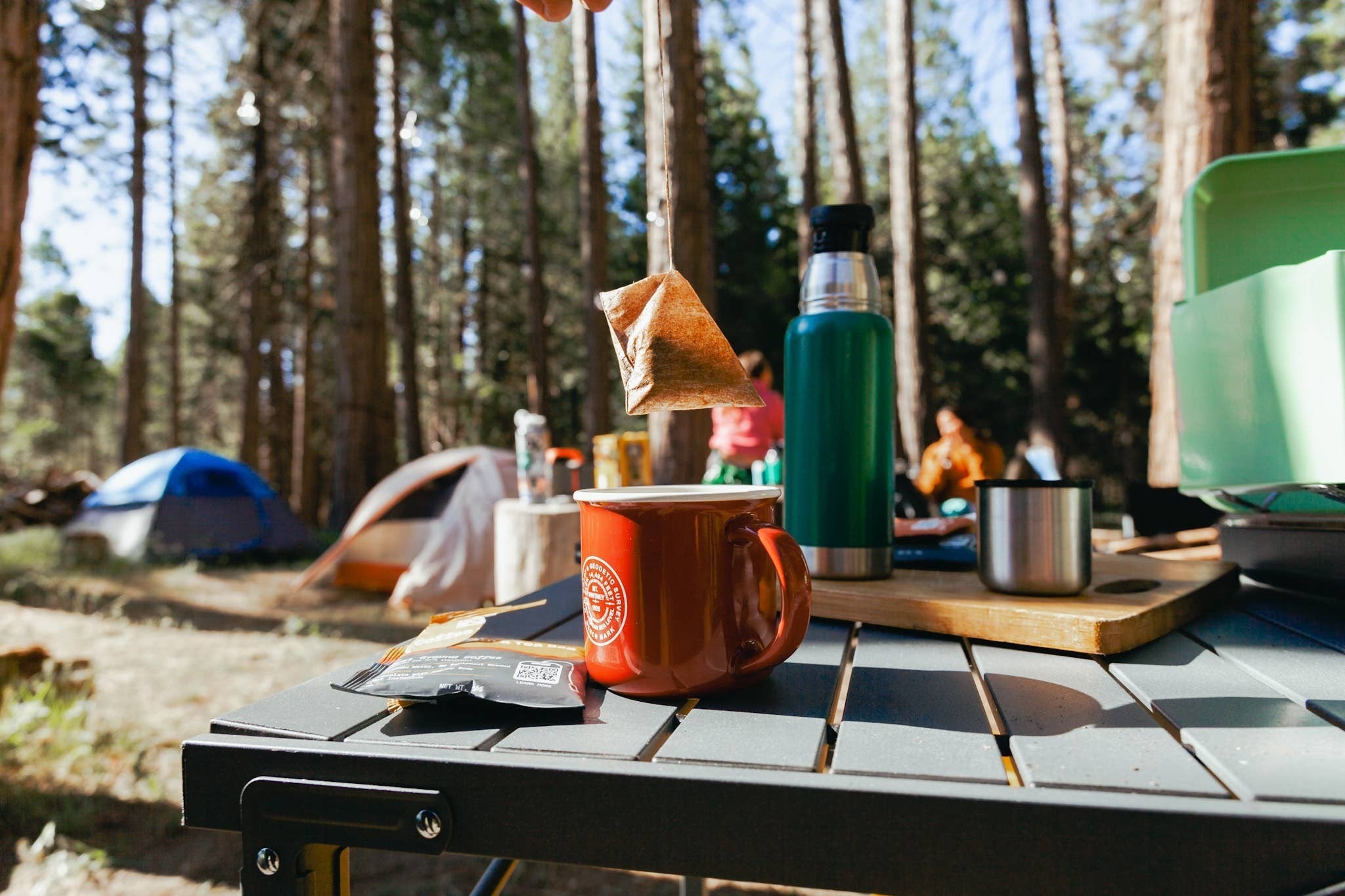 The Hocking Hills Store Wildland Coffee extra dark roast steepable coffee bag being lowered into a red camping mug outdoors.