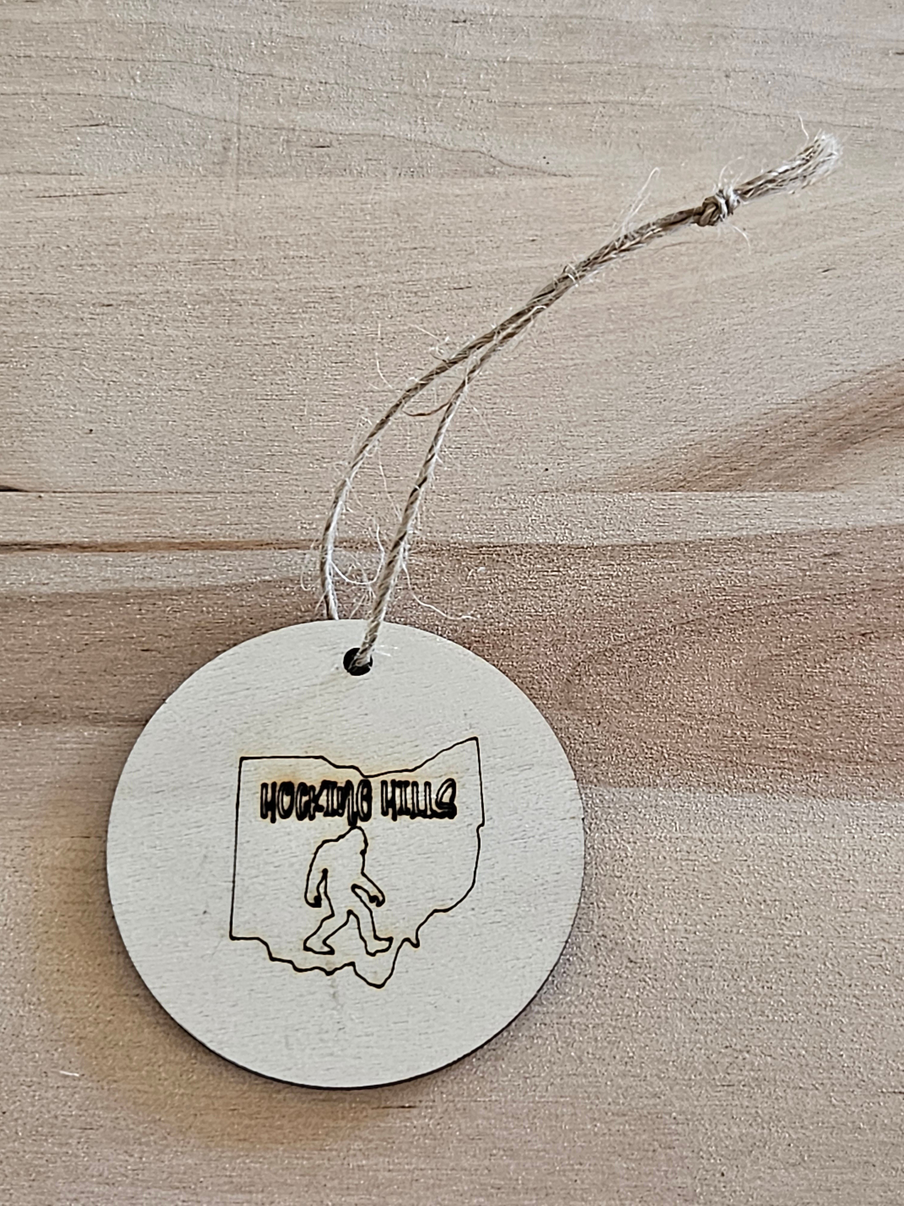 The Hocking Hills Store wood engraved round ornament featuring Bigfoot silhouette inside Ohio outline with Hocking Hills text.
