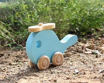 The Hocking Hills Store light blue handmade wooden toy helicopter with natural wood wheels and propeller, set on the ground.