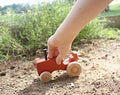 The Hocking Hills Store handmade wooden toy tractor, red with natural wood wheels, held by a child's hand outdoors.
