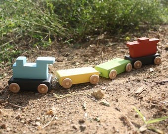 The Hocking Hills Store handmade wooden toy train set with blue engine, yellow, green, and red carriages on dirt.