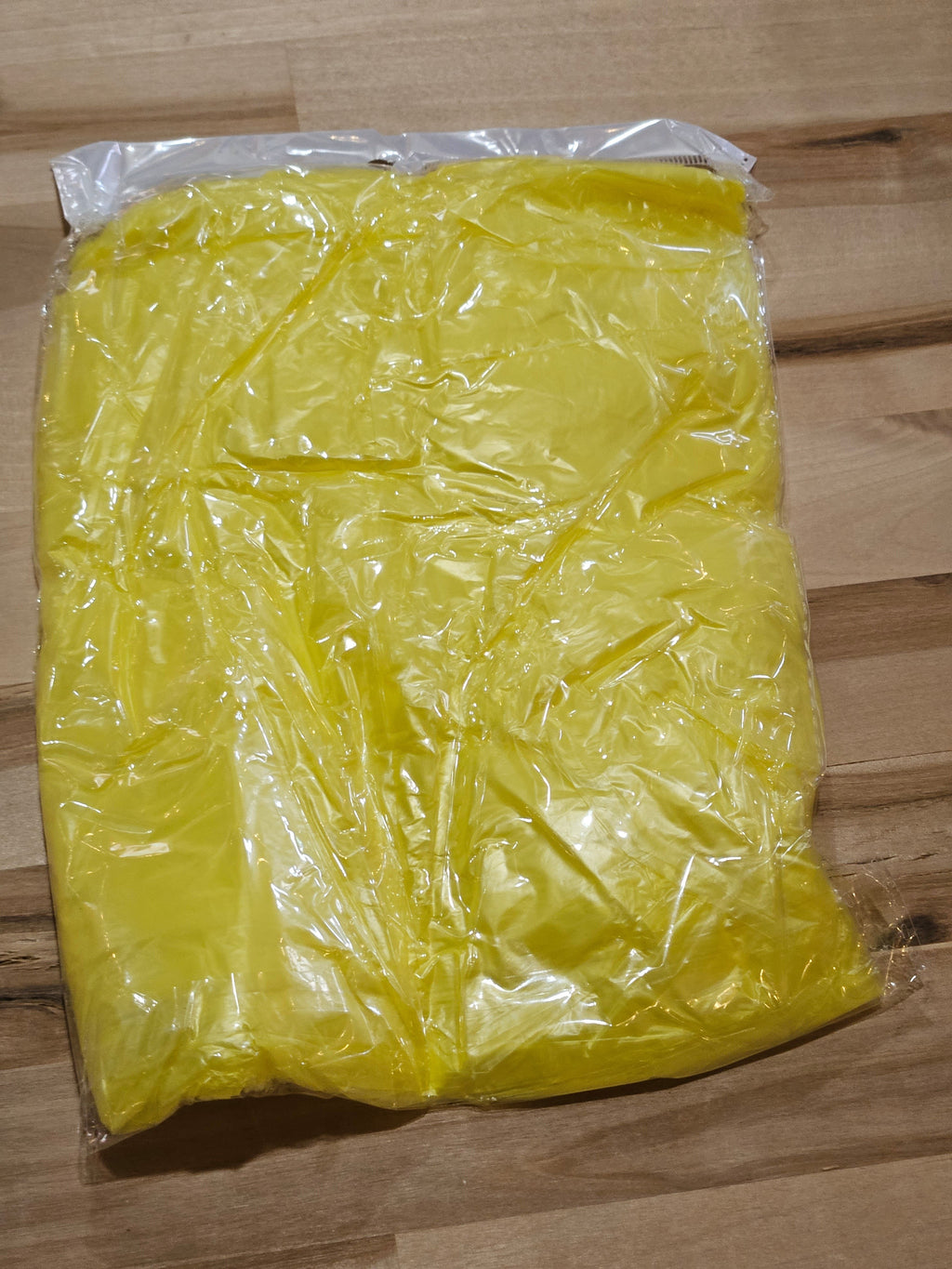 The Hocking Hills Store yellow disposable emergency rain poncho in clear plastic packaging on a wooden surface.