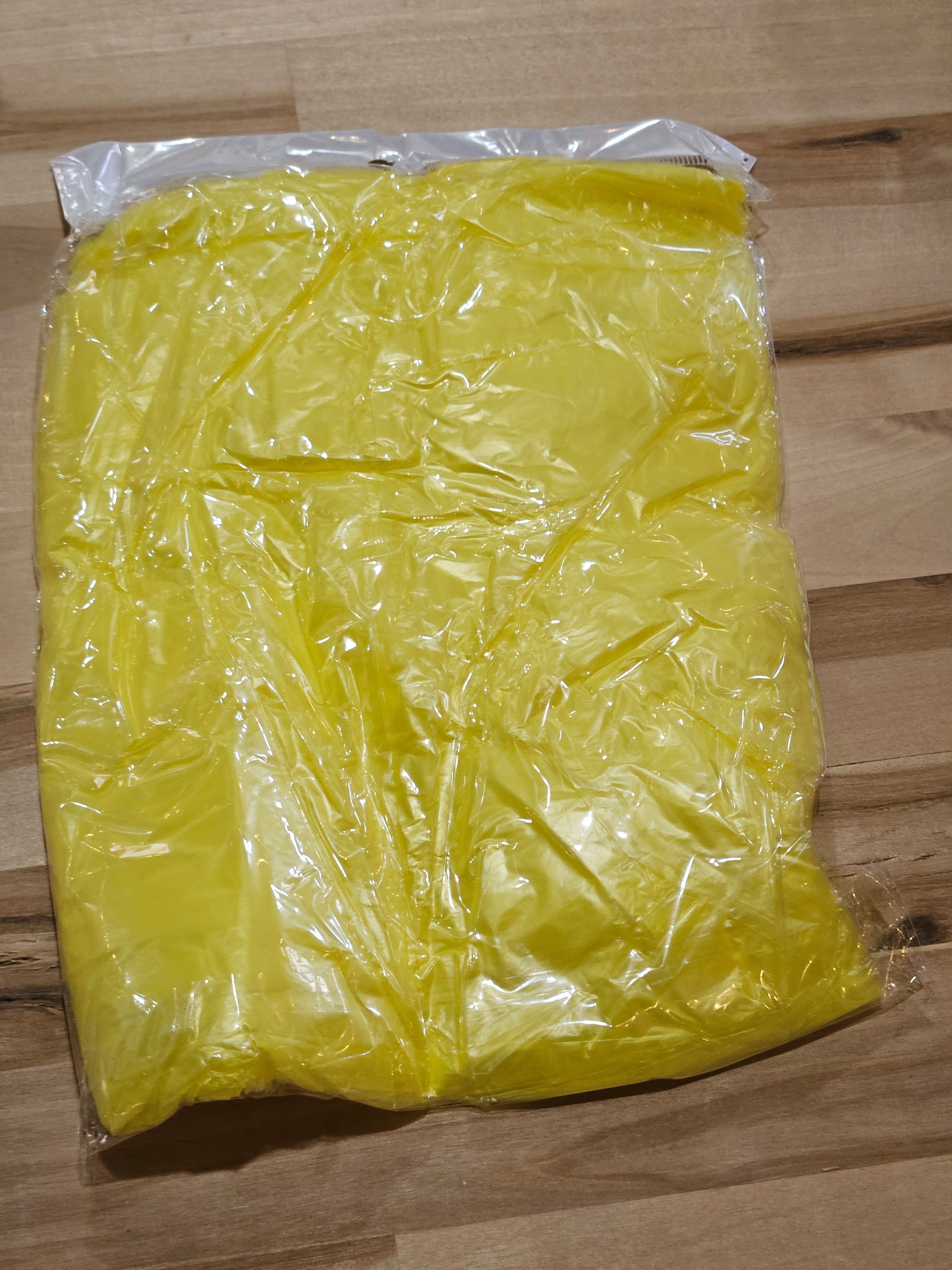 The Hocking Hills Store yellow disposable emergency rain poncho in clear plastic packaging on a wooden surface.